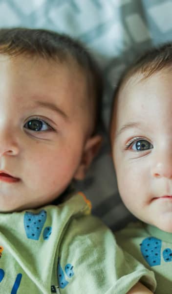 twin babies, in cute matching jumpsuits, with bright eyes