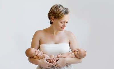 A mother, tenderly holding her sleeping twin babies, cradling them in each arm.