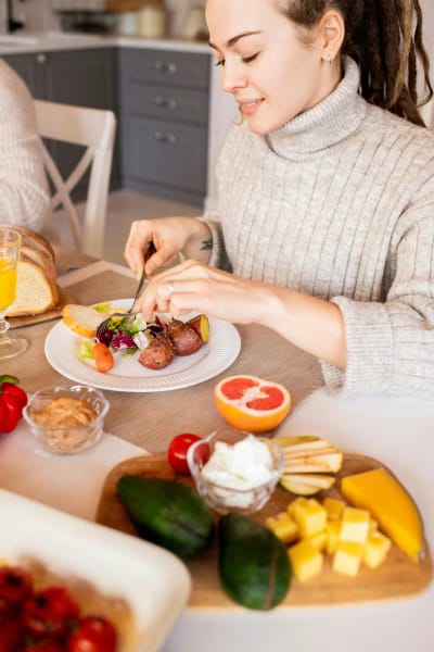 An attractive woman cutting up fruit at a dining table with a friend, enjoying the healthy snack.