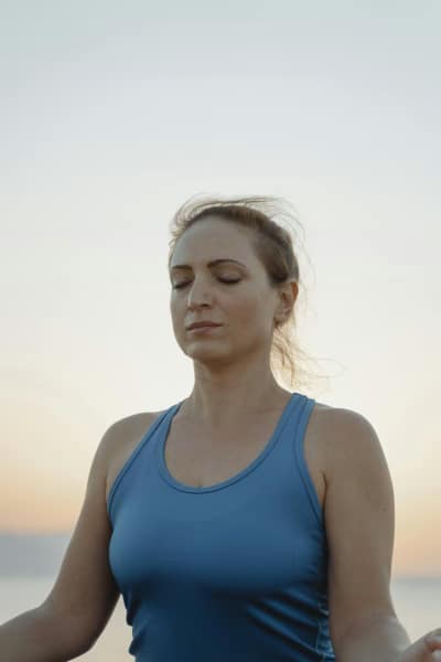 A woman meditating in peaceful surroundings, with her eyes closed, and a breeze in her hair.