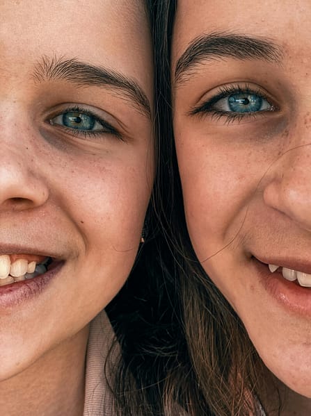 Intimate close-up of two smiling twin girls with blue eyes, capturing joy and connection.
