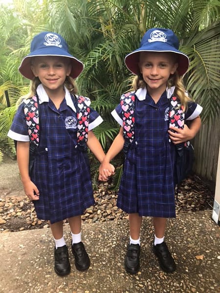 Twins in the same class, holding hands and smiling, wearing matching school uniforms.