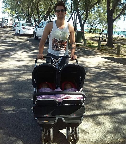 A father, pushing a double stroller with twins, by the beach, in a park