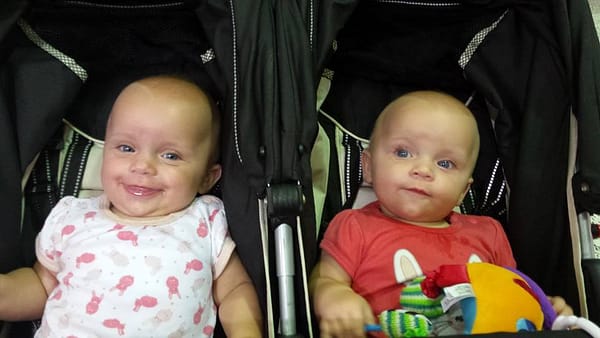 Cute newborn twins, sitting in a pram, one laughing at the other.