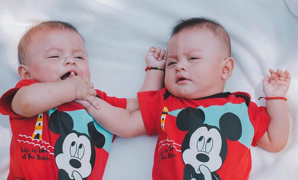 Cute twin babies wearing matching red t-shirts enjoying a moment indoors.