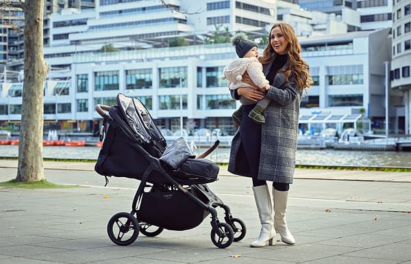 A woman gently pushes a stroller, cradling a baby, showcasing a tender moment of motherhood in a serene setting.