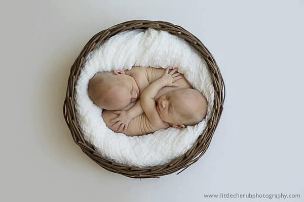 Beautiful Identical Mirror Twins as babies in a round bassinet.
