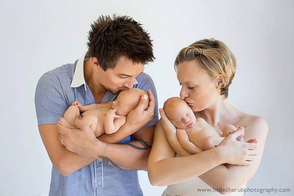 A father and mother, holding their neborn twins, tenderly kissing there heads.