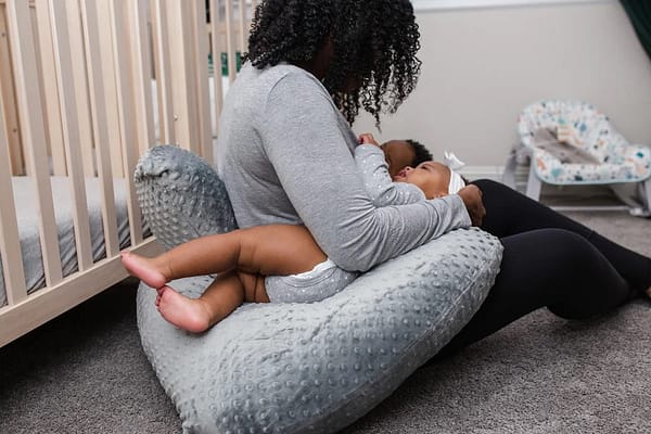A mom sitting on the floor, with her twin babies resting on a twin nursing pillow.