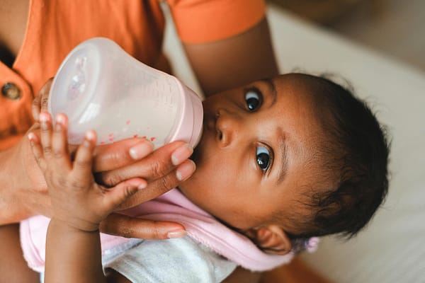 A baby girl with big eyes, enjoying a bottle of milk from her mother