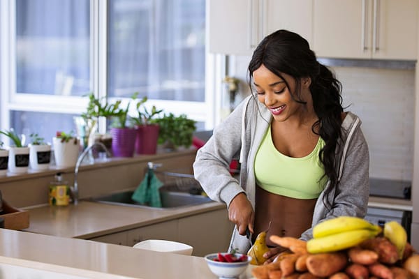 a happy, fit woman happily chopping up fruit in the kitchen