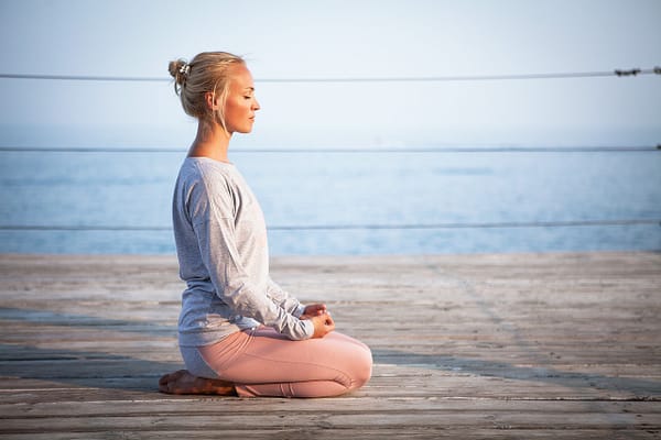 A woman practicing yoga on a pier, by the ocean, at peace, with her eyes closed.