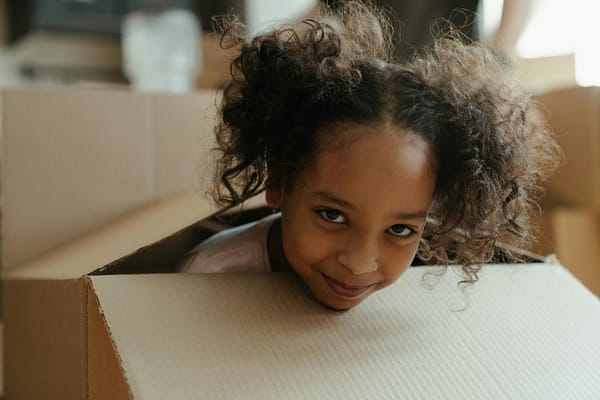 A playful child with curly hair inside a cardboard box