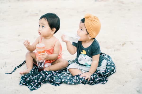 Cute twin babies, sitting on the sand together playing.
