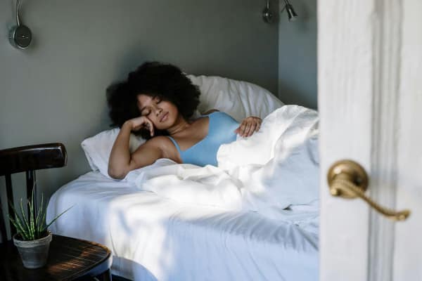 A woman lying in bed, resting, almost asleep, in white bed sheets.