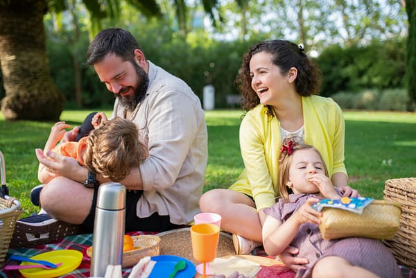 A happy family of four, enjoying a picnic on the grass, in the park, on a lovely sunny day.
