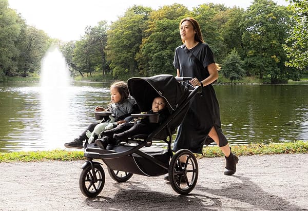 A woman happily pushes children in a stroller, in a sunny park.