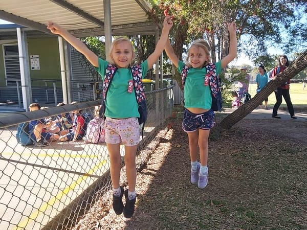 Twins in the same class, jumping for joy in a school yard.
