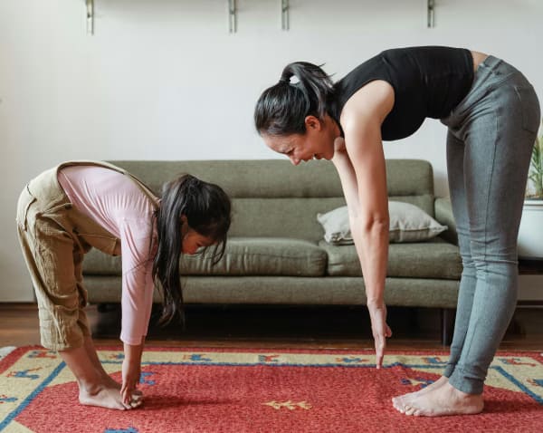 An Asian mother and daughter happily performing stretching exercises in a living room.