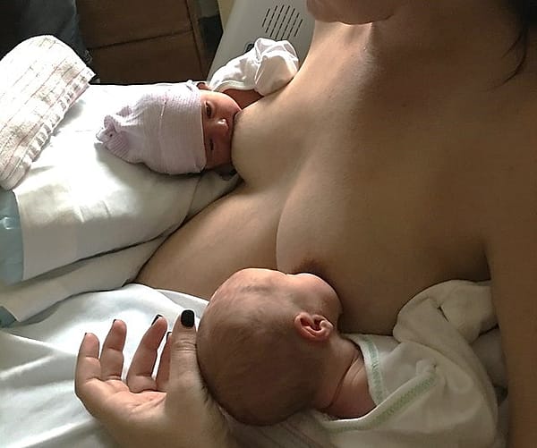 A mother in a hospital bed nursing twins for the first time