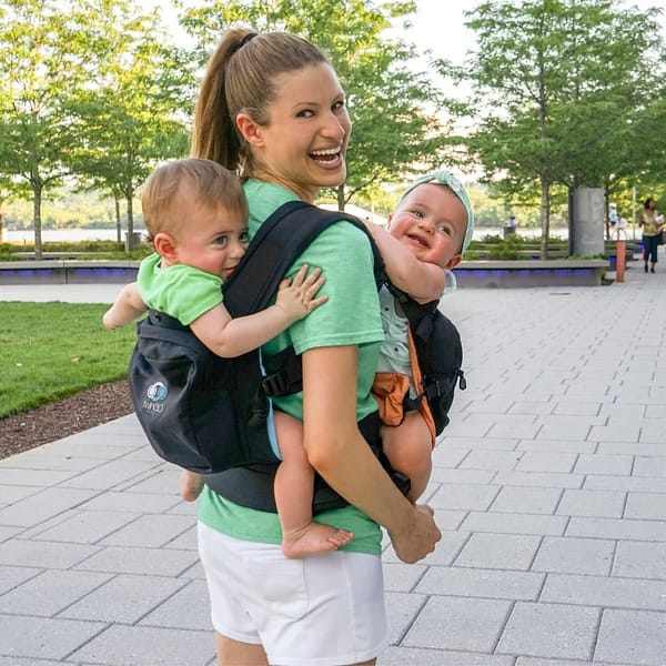 woman wearing a baby carrier, holding two infants close to her chest, showcasing a nurturing and caring moment.