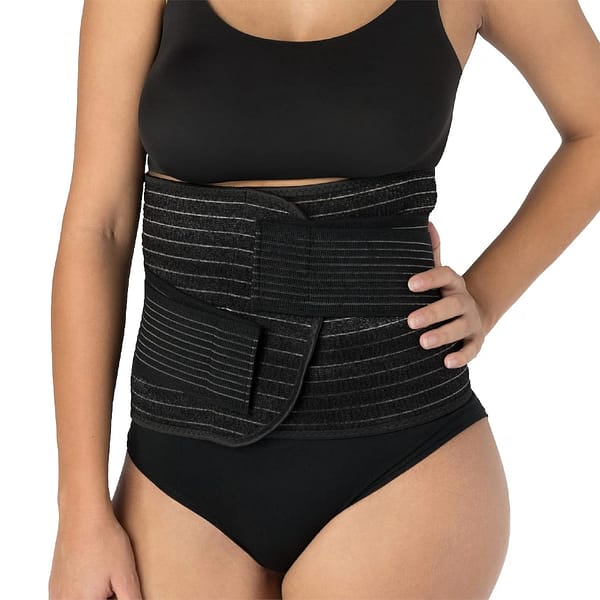 A woman standing with hand on hip, displaying a black Postpartum Belly Wrap.
