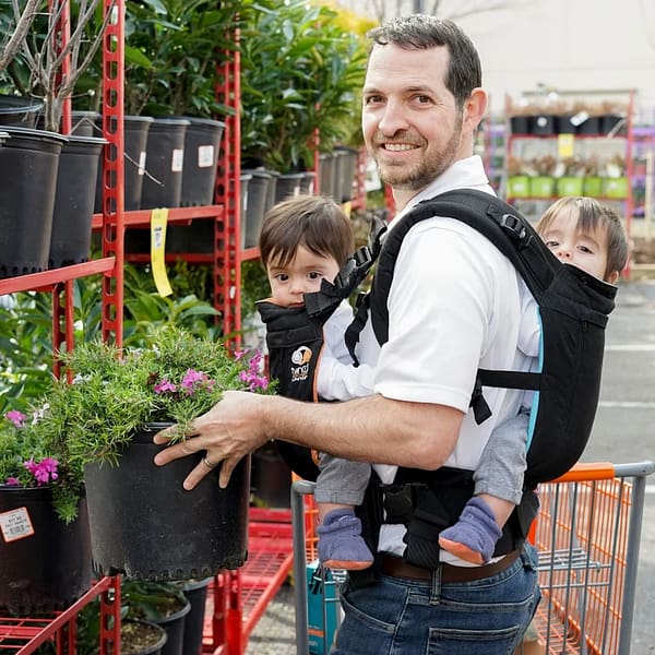 A happy father carrying his twin babies, while selecting a pot plant in a garden nursery.
