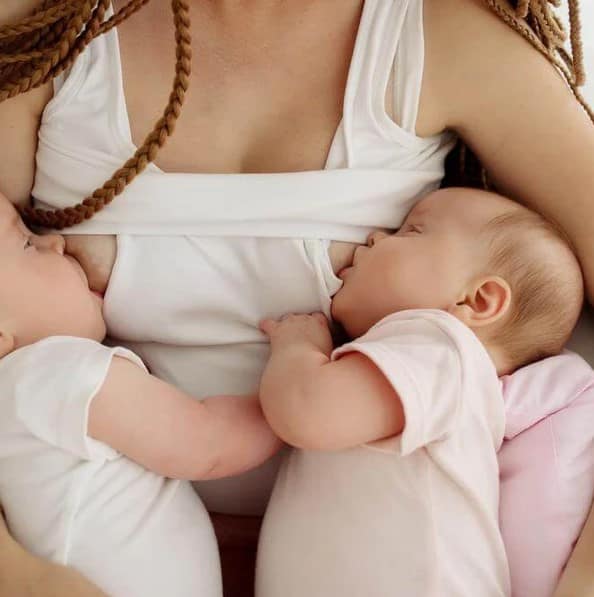 A caring mother, nursing twins, holding them close in her arms, showcasing a tender moment of bonding.